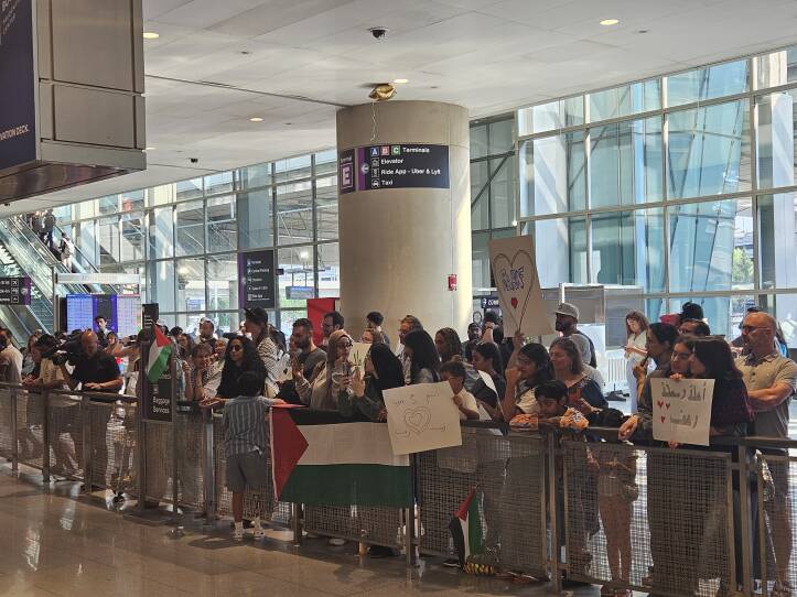 A group of people hold signs in English and Arabic. Some hold Palestinian flags.