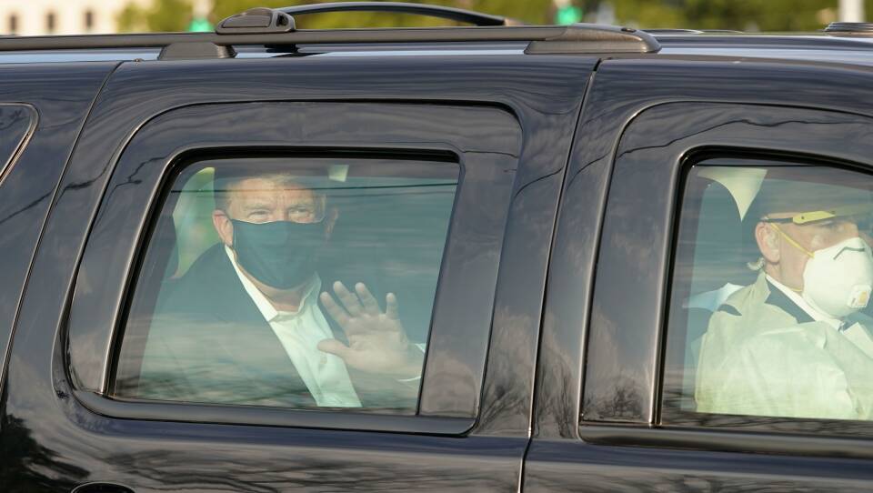 President Trump waves from a motorcade outside Walter Reed Medical Center, accompanied by Secret Service agents on Sunday.