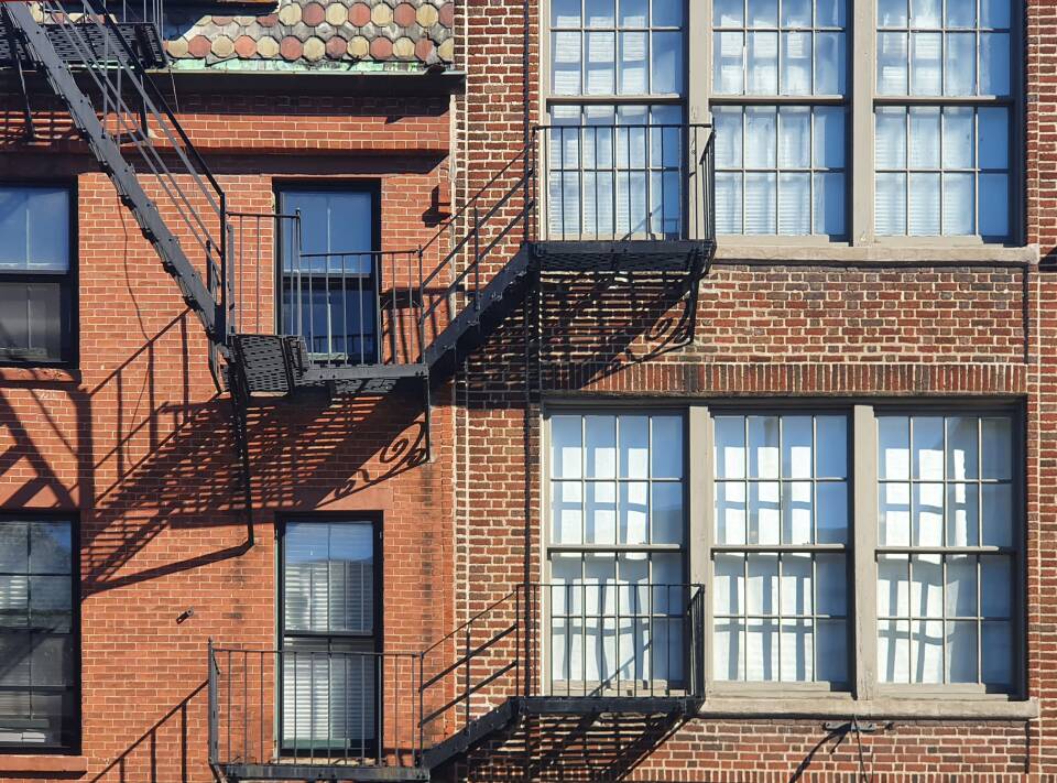 Two brick buildings nestled together with black iron fire escapes.