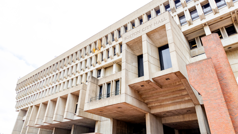 A large brutalist-architecture building with the words "Boston City Hall" over the doorway windows.