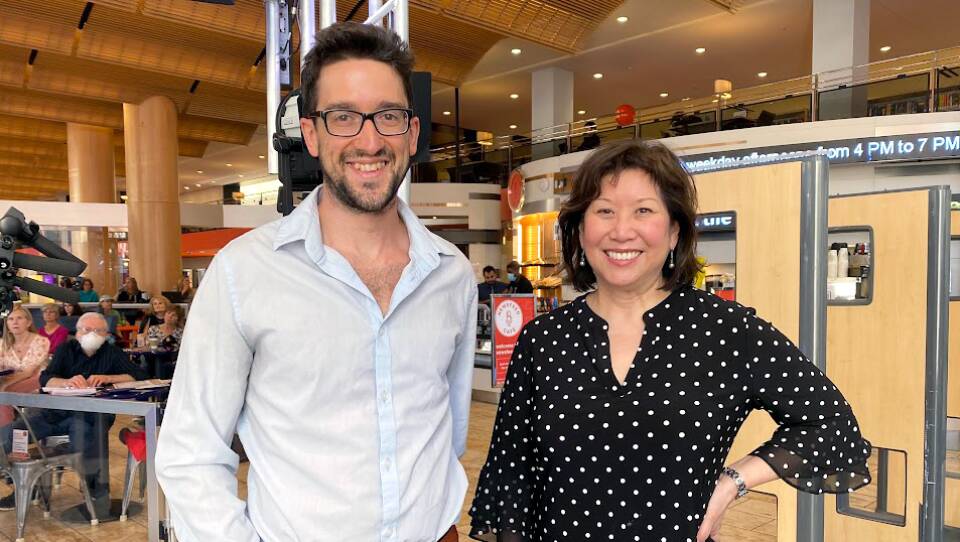 A man with a light blue button-down stands with a woman in a polka dotted black and white blouse, both smiling for the camera