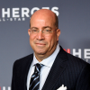 A man wearing glasses and half smiling stands in a pinstripe suit in front of a wall that reads "CNN HEROES: AN ALL-STAR TRIBUTE"
