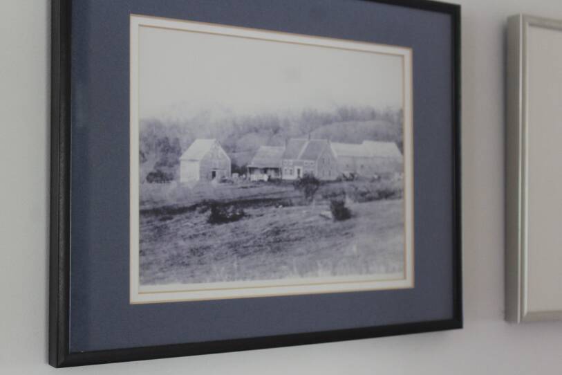 A framed black-and-white photograph of a farm home and surrounding buildings hangs on a wall.