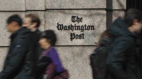 Several people walk past a building with a sign for The Washington Post.