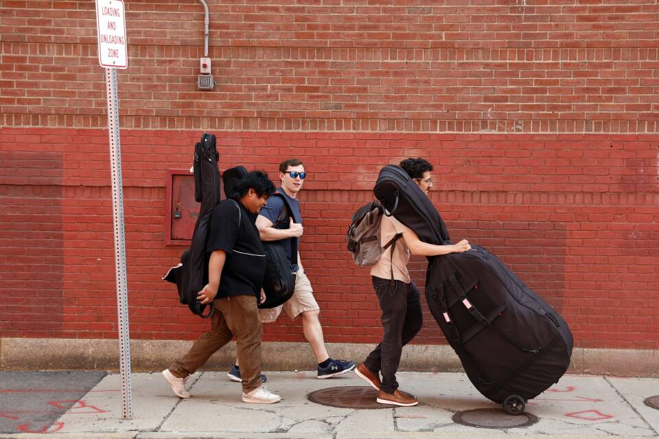 Three students carry instruments down the sidewalk.