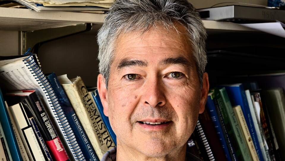A man in a plaid shirt poses in front of a metal bookshelf.