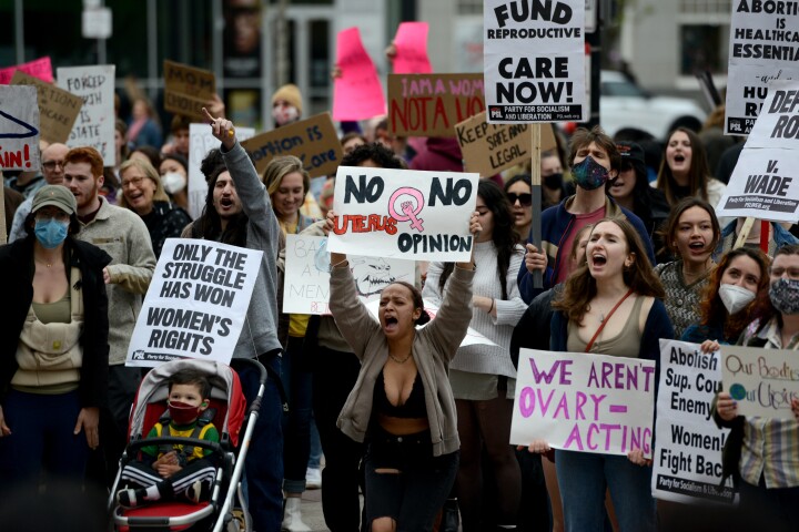Dozens of protesters waving signs and shouting are shown in an image from a pro-choice protest in Boston. Handmade signs include slogans "No Uterus No Opinion" and "We Aren't Ovary-Acting".