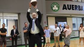 Charlie Baker jumps and throws a basketball wearing a suit.