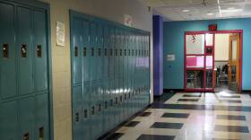 Lockers line the wall of a school hallway, with a classroom open on the other side.