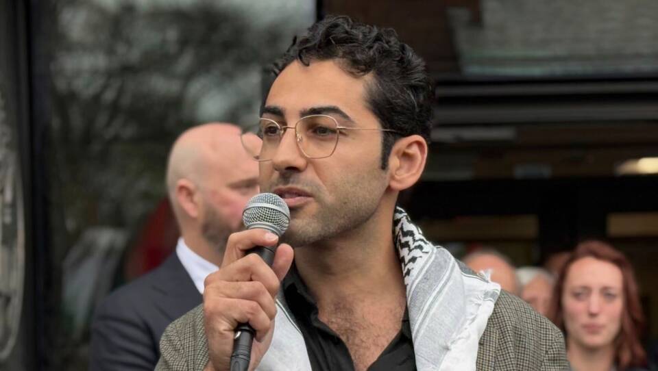 A young man in a keffiyah speaks into a microphone outside a courthouse.