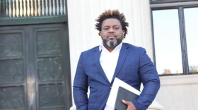 A man in a blazer stands on government building steps