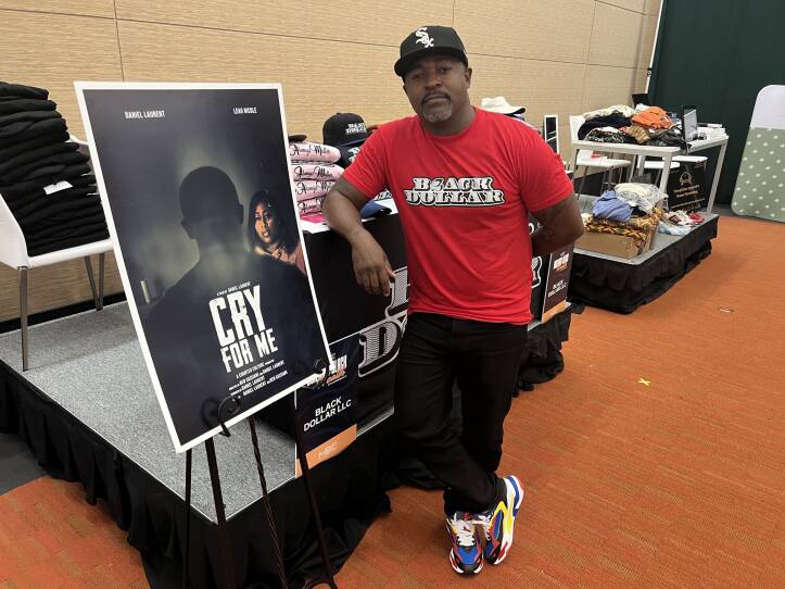 A man leans against a table next to a movie poster for a film called "Cry for Me" that has a woman looking fearfully at a man whose face is not visible.