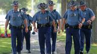 A group of uniformed state police officers walk down a sidewalk