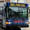 A blue bus turns around the corner of a city street on a rainy day.