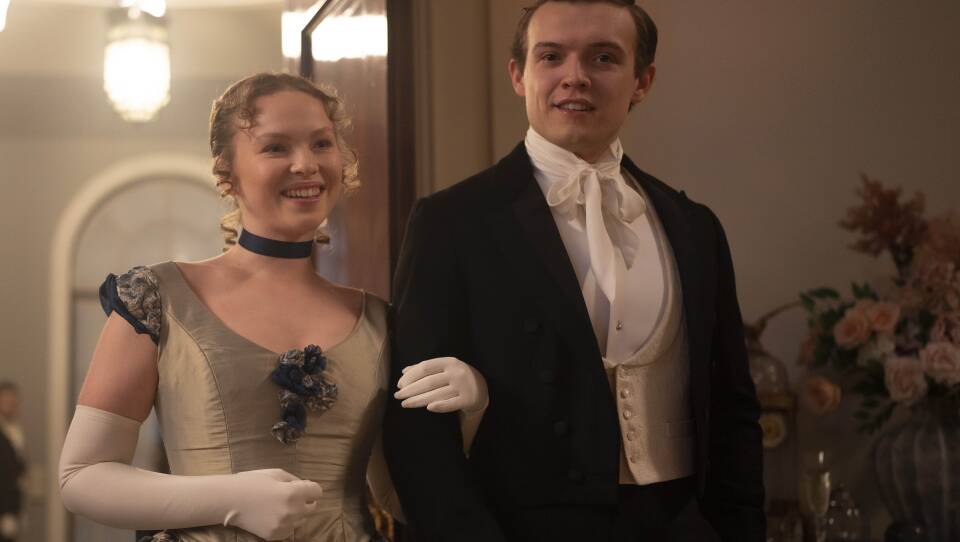 Shown from left to right: Laura Marcus as Young Eliza and Matt Olsen as Young William. The teens, dressed in party clothes, enter a soiree.