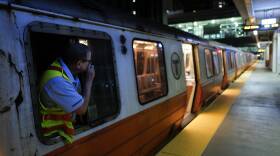 A subway train at night, with a conductor leaning out of a window speaking into an intercom.