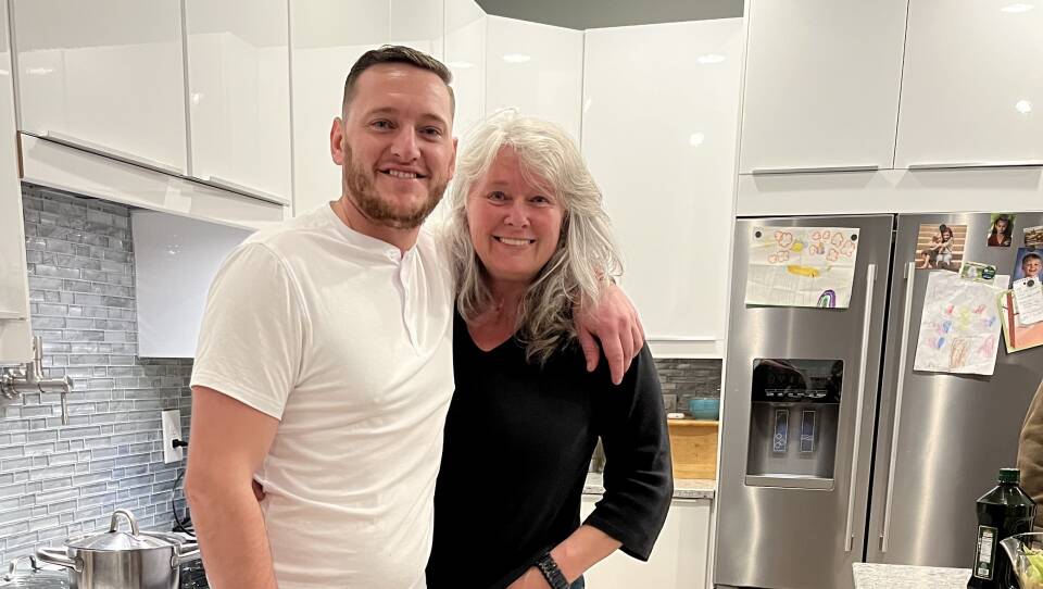 A man and a woman stand in a kitchen, smiling.