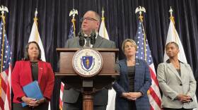 A white man in glasses stands at a lectern bearing the Massachusetts seal.