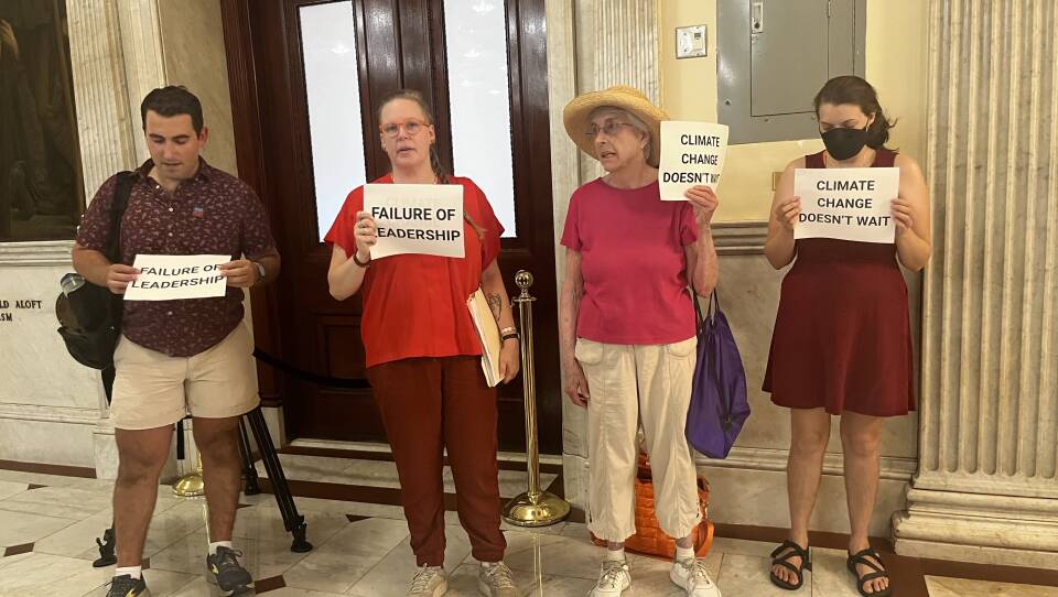 Four people stand in a marble hall, holding signs that say "failure of leadership" and "climate change doesn't wait"