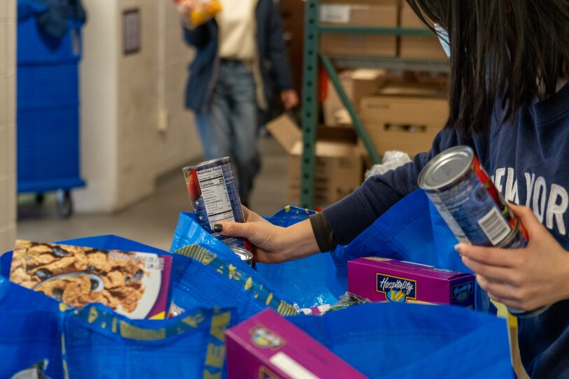 A woman puts canned goods into large reusable grocery bags, which already have other groceries like cereal boxes peeking out.