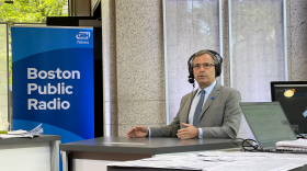 A man in a suit and a radio headset looks serious while speaking from the Boston Public Radio set.