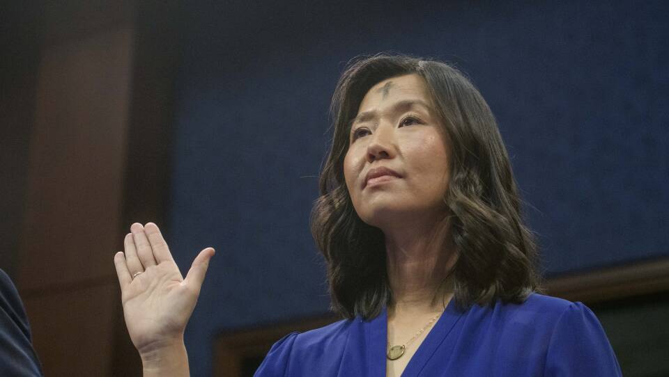 A woman with an ash cross on her forehead and a serious expresses raises one hand as she takes an oath.
