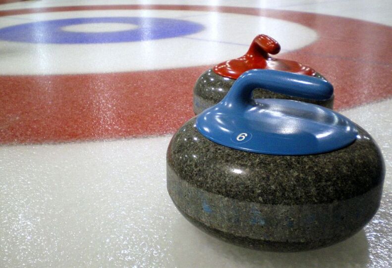 This is an extreme close up of two curling stones on an ice rink. One curling stone has a blue handle, the other one has a red handle.