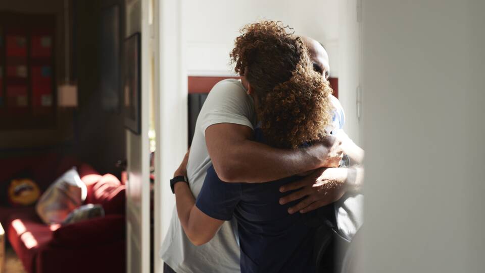 Rear view of female caregiver embracing while greeting man at home