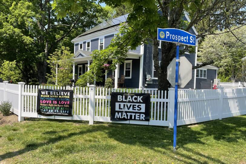 Black Lives Matter signs hang on a white fence in front of a blue house.