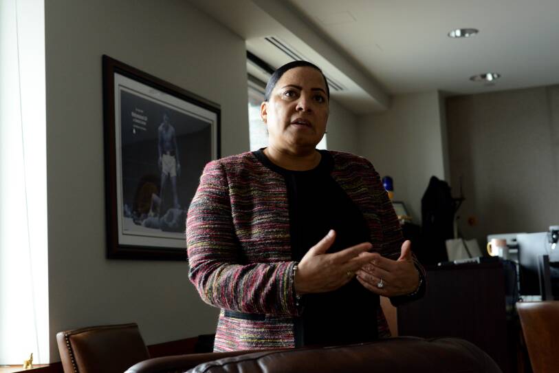 A woman stands in an office, her hands gesturing as if she's speaking with someone.