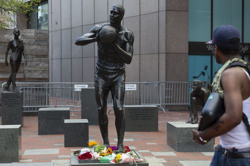 A bronze statue of a man in a Celtics uniform holding a basketball, with flowers placed near its base.