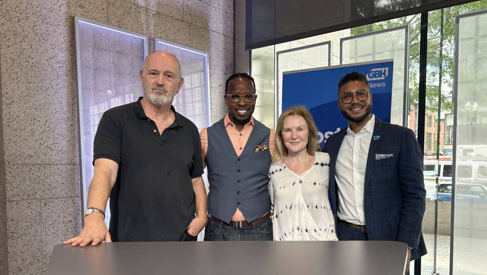 Four people smile as they stand with arms wrapped behind one another's backs.