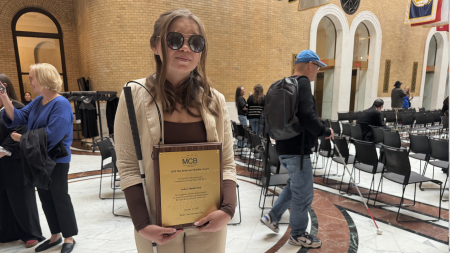 A woman wearing sunglasses holds a white and a bronze plaque.