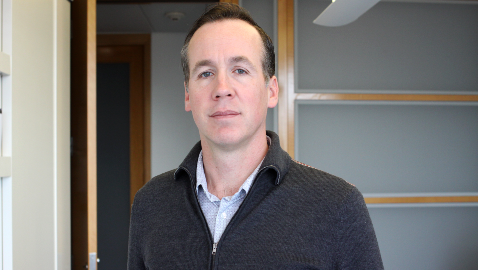 A man in a collared shirt and a quarter-zip poses neutrally for the camera