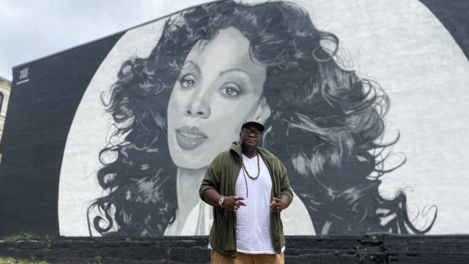 A man stands in front of a massive black-and-white mural of a woman.