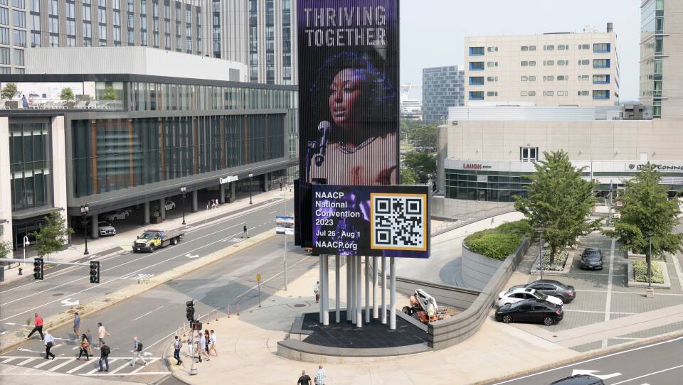 A city street with a large electronic billboard advertising the NAACP National Convention, July 26-Aug. 1.