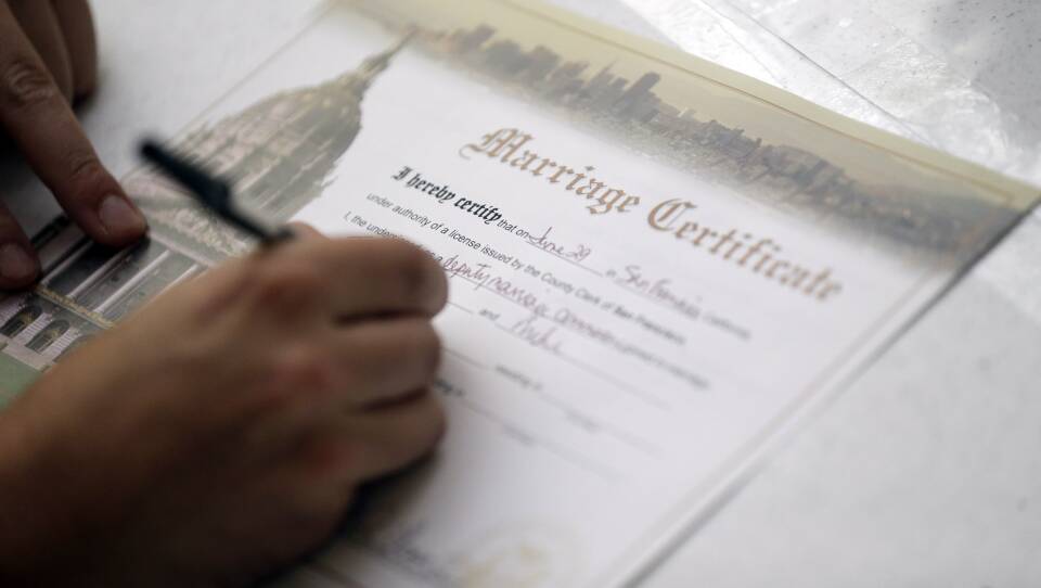 A white and gold marriage certificate is being filled out.