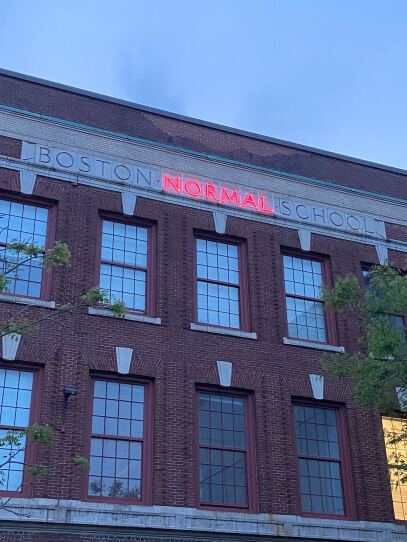 Bright neon lights up the word "Normal" in MassArt's original title "Boston Normal School"