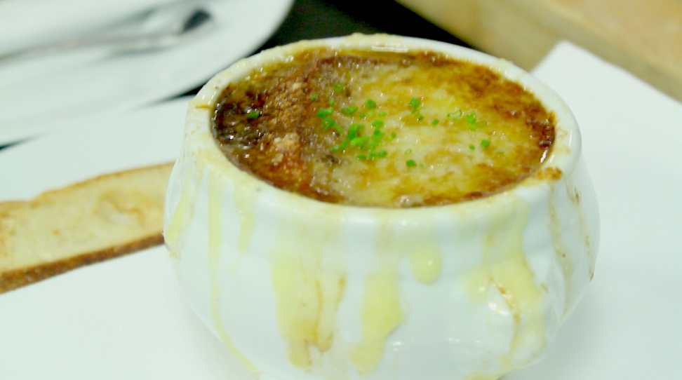 A white bowl of french onion soup with cheese dripping down the side