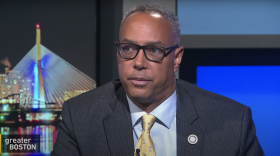 A screenshot of Kevin Hayden on Greater Boston, wearing a suit in a TV studio.