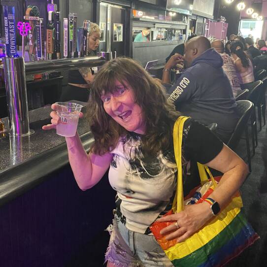 A woman holding a drink near the bar at Dani's Queer Bar.