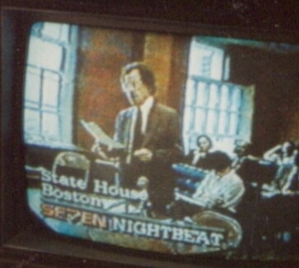 A grainy shot of a man speaking to legislators
