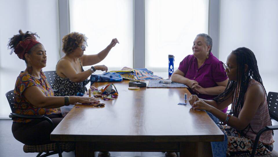 Four women sit around a rectangular table as they sew and talk.