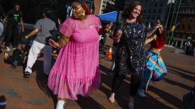 People in colorful clothing dance on a brick plaza.