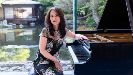 Yoko Miwa wears a flower patterned dress, and sits at a grand piano in front of beautiful garden with pond.