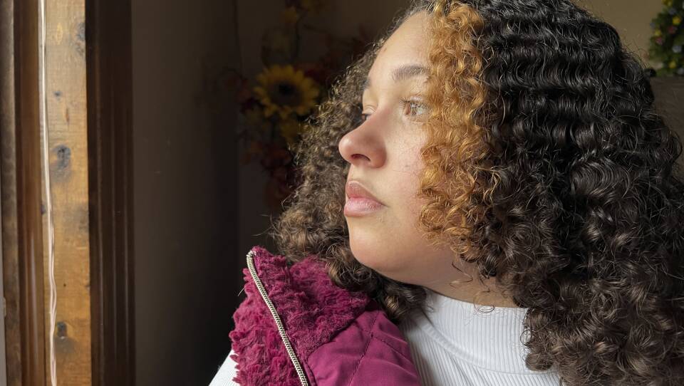 A young woman looks out a window, with the sunlight shining on her face.