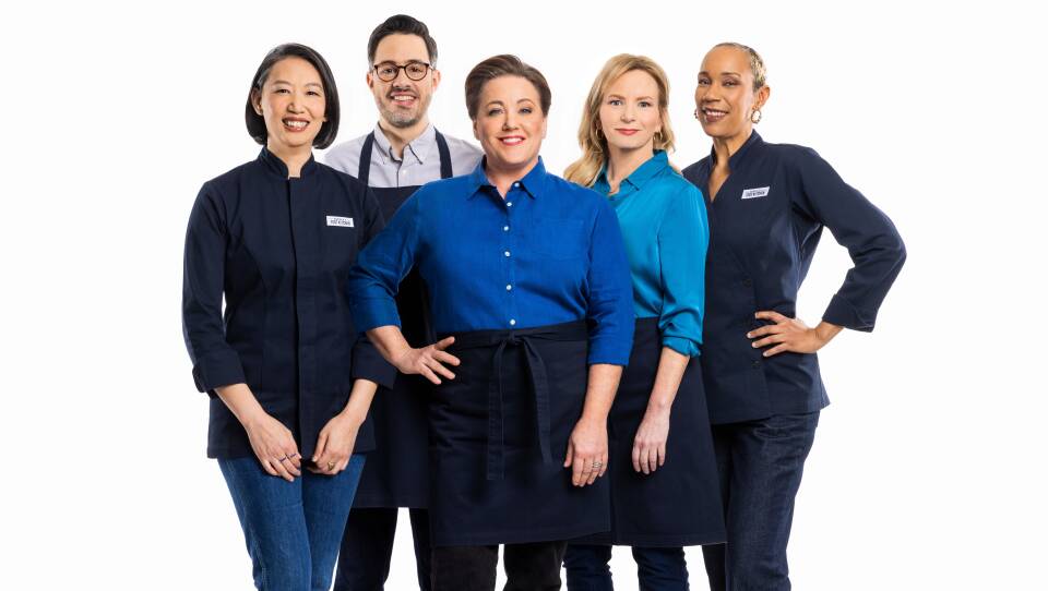 Group of four women and one man posing wearing aprons and chef's coats
