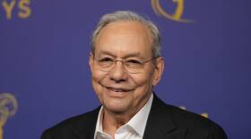Lewis Black smiles as he stands in front of a backdrop for the Emmys on the red carpet.