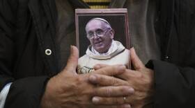 A person clasps their hands to their chest over a photo of the Pope