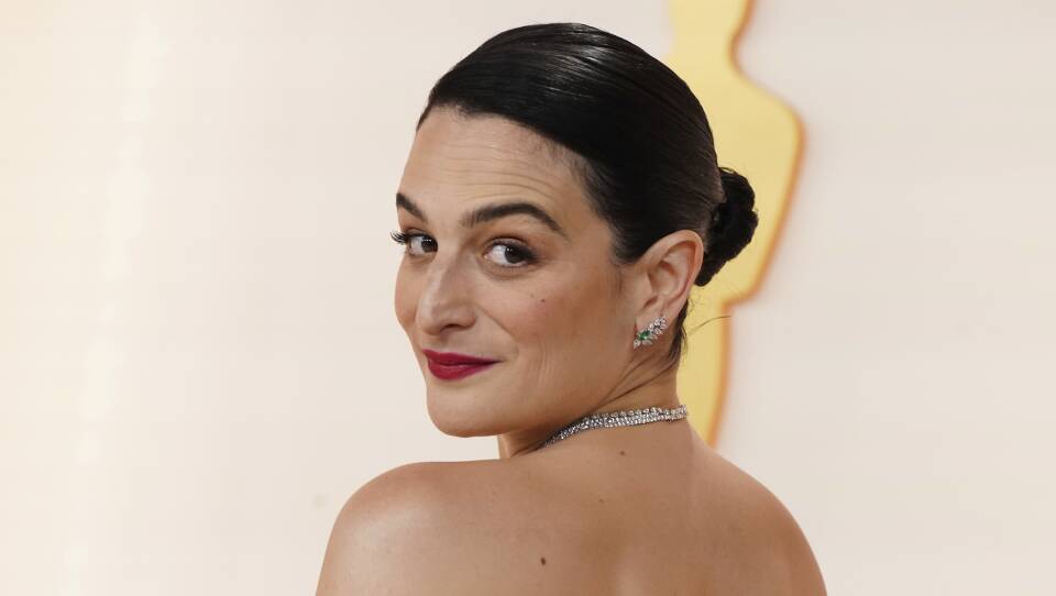 Jenny Slate smiles as she peers over her shoulder on the Oscars red carpet.